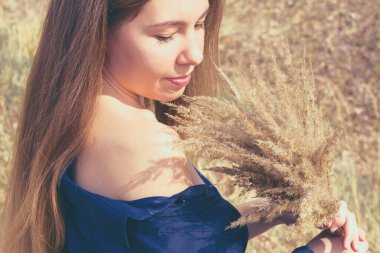 Parlak sonbahar güneşinde uzun ipek gibi sarı saçlı genç bir kadın. Sazlık buketi tuttuğu için omuzlarında gölgeler var. Sonbahar ya da saç bakımı kavramı, kurumuş hasarlı saç..