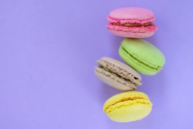 Dört sarı, pembe, kahverengi ve pembe bisküvi. Biri diğerinin üstünde. Fotokopi alanı olan menekşe arkaplan üzerinde. Geleneksel Fransız pastanesi, üst manzara