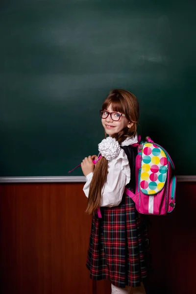 Backpack behind the girl in school uniform. Educational class, chalk board green.