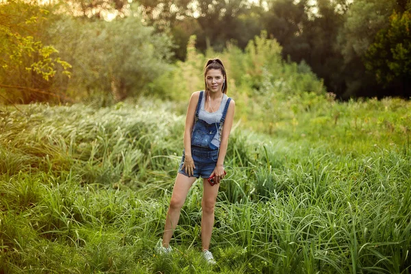 girl in headphones dancing in denim overalls. Out in the park