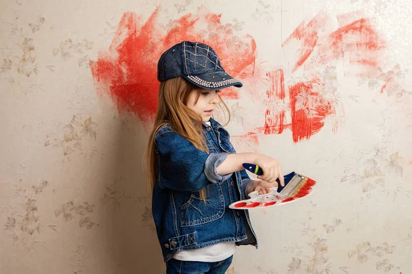 a girl with a paint roller and red paint in her hands draws on the wallpaper in the room. Hooliganism and prank