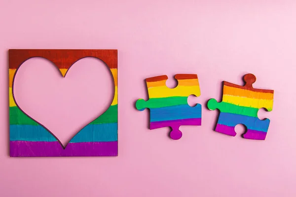 mock-up LGBT symbolism in the form of a rainbow two puzzle and heart frame. A place for photography and text on a pink background.