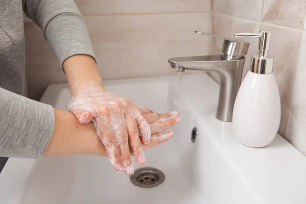rules of hand washing. A woman washes her hands between her fingers with liquid soap under a tap of water in the bathroom.