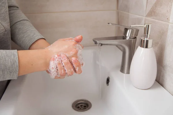 rules of hand washing. A woman washes her hands between her fingers with liquid soap under a tap of water in the bathroom.