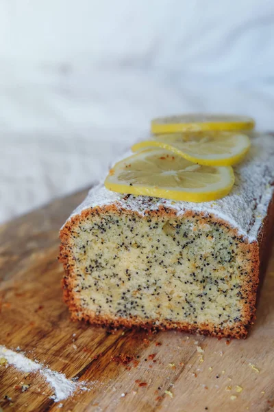 Cake with poppy seeds and lemon zest, sprinkled with powdered sugar. Cupcake with lemon on a wooden board. — Stock Photo, Image