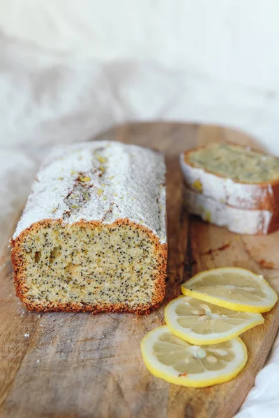 Cake with poppy seeds and lemon zest, sprinkled with powdered sugar. Cupcake with lemon on a wooden board. — Stock Photo, Image