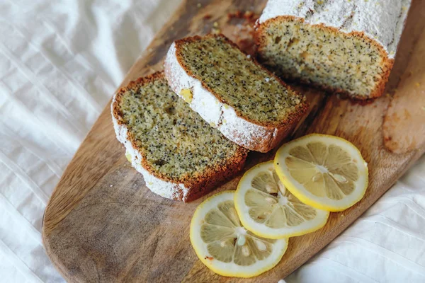 Cake with poppy seeds and lemon zest, sprinkled with powdered sugar. Cupcake with lemon on a wooden board. — Stock Photo, Image