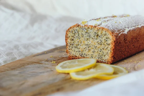 Cake with poppy seeds and lemon zest, sprinkled with powdered sugar. Cupcake with lemon on a wooden board. — Stock Photo, Image