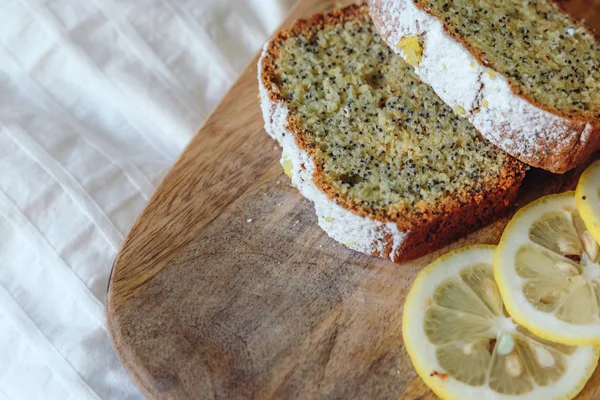 Cake with poppy seeds and lemon zest, sprinkled with powdered sugar. Cupcake with lemon on a wooden board. — Stock Photo, Image