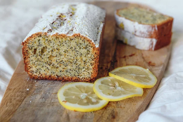Cake with poppy seeds and lemon zest, sprinkled with powdered sugar. Cupcake with lemon on a wooden board. — Stock Photo, Image