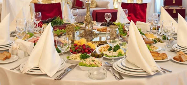 Kutlama masası, servis. Masa ayarı. Tabaklar, bardaklar, yiyecekler, salatalar, meyveler masada..