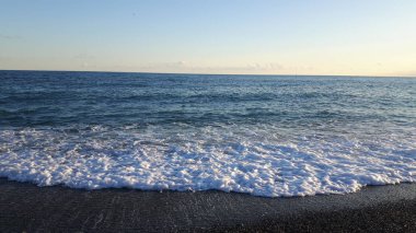 Güzel bir mavi denizi, küçük dalgalar ve sümer gün içinde gizli bir günbatımı horizzon üzerinde inanılmaz bir resim yazısı