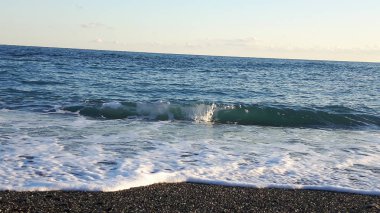 Güzel bir mavi denizi, küçük dalgalar ve sümer gün içinde gizli bir günbatımı horizzon üzerinde inanılmaz bir resim yazısı