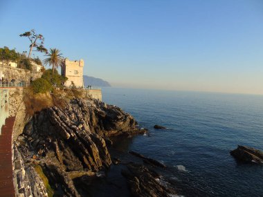 Genova, İtalya - 15.03.2019: Güzel kırmızı ve mavi gökyüzü, arka planda bazı şaşırtıcı bulutlar ve deniz üzerinde eski kayalar ile Genova denizi üzerinde bahar günlerinde gün batımı inanılmaz bir başlık.