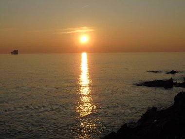 Genova, İtalya - 15.03.2019: Güzel kırmızı ve mavi gökyüzü, arka planda bazı şaşırtıcı bulutlar ve deniz üzerinde eski kayalar ile Genova denizi üzerinde bahar günlerinde gün batımı inanılmaz bir başlık.