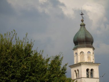 Tarzo, İtalya - 08 / 15 / 2020: Yaz günlerinde İtalya 'nın kuzeyinden gelen küçük bir köyün güzel fotoğrafları. Eski kiliseye, dağlara ve arka planda gri ve mavi gökyüzü olan bazı evlere bakın..