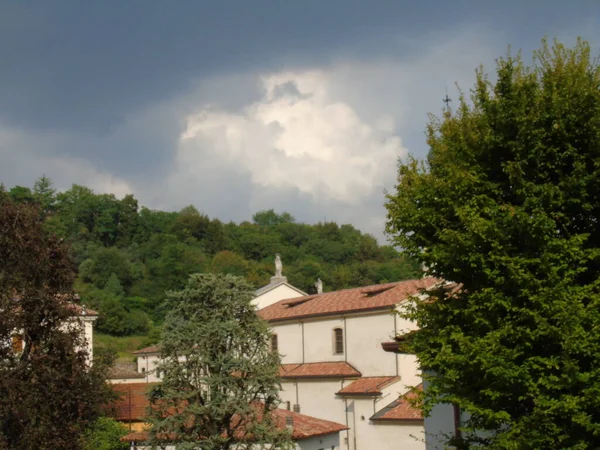 Tarzo, Italy - 08/15/2020: Beautiful photography of a little village from north Italy in summer days. View to the old church, mountains and some houses with grey and blue sky in background.