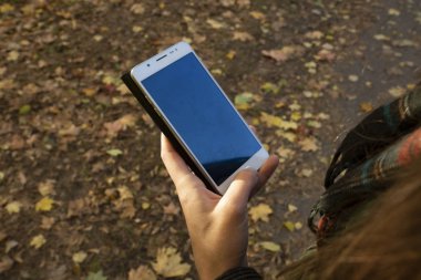 Sonbahar parkta kız telefonu elinde tutar.