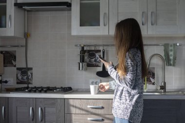 Mutfakta çay içen ve telefonda mesaj okuyan kadın