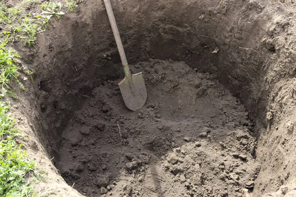 Deep pit in the ground. In the pit lies a shovel. Digging a hole.