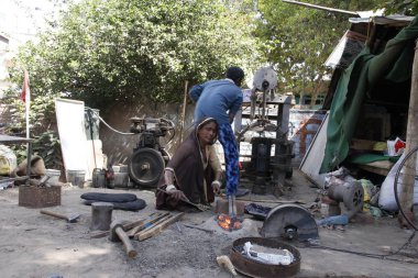 Delhi/Hindistan-Mart 22 2019: Hintli aile sanat Demircilik meşgul. Bir kadın Forge 'da kırmızı-sıcak bir metal tutuyor. Aile çadırda yaşıyor..