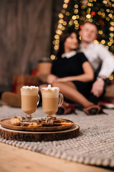two cups of cocoa on the background of a couple in love sitting near a Christmas tree