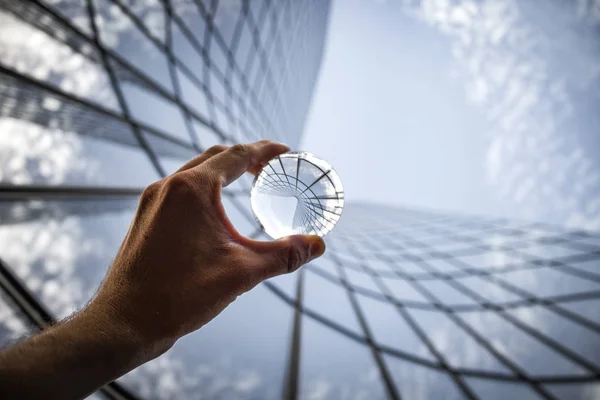 glass building facade and partial view of hand holding glass sphere