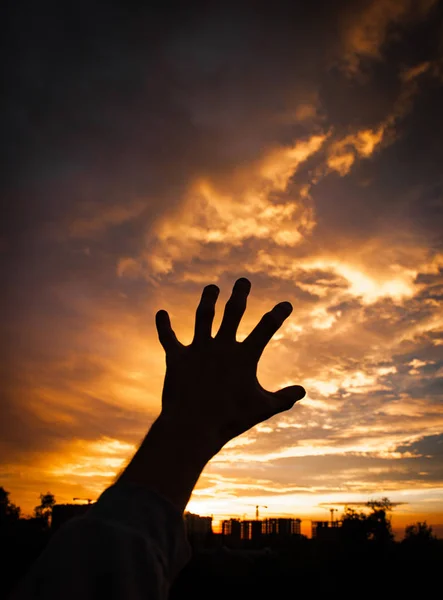 sunset sky with clouds and silhouette of human hand