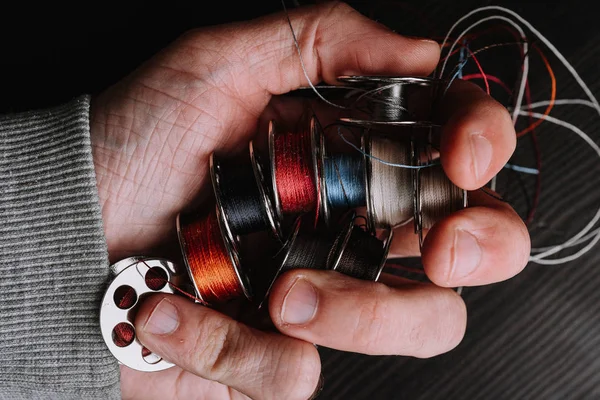 cropped image of male hand holding sewing machine threads coils