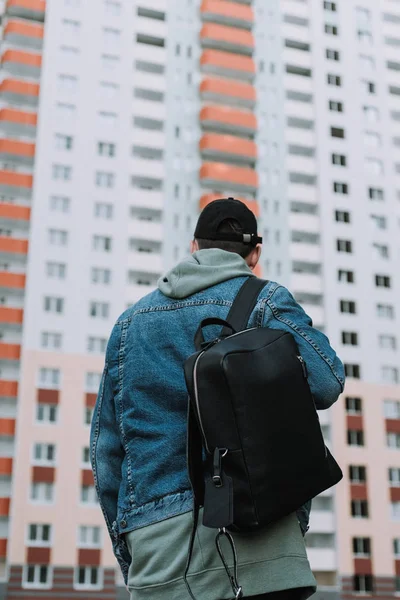 back view of standing man with backpack and cap at residential building
