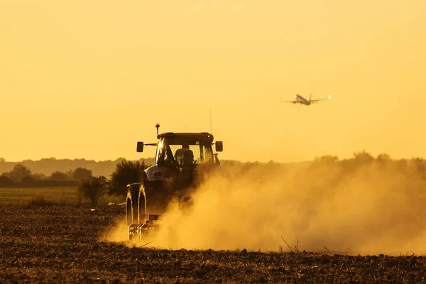 Moderní Traktor Orat Při Západu Slunce Množstvím Prachu Pozadí Letadlem — Stock fotografie