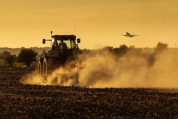 Современный Трактор Вспахивающий Закате Большим Количеством Пыли Заднем Плане Самолетом — стоковое фото