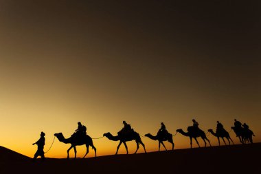 Sillhouette mutlu peopple ile arka planda kızıl gökyüzü gün batımında çölde gidiş ile deve karavan