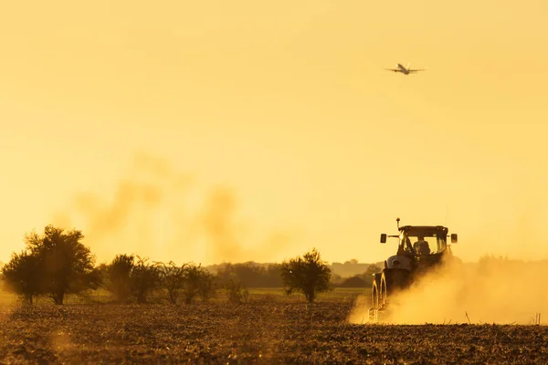 近代的なトラクターで耕夕暮れ背景にほこりの多いと飛行機の離陸 — ストック写真