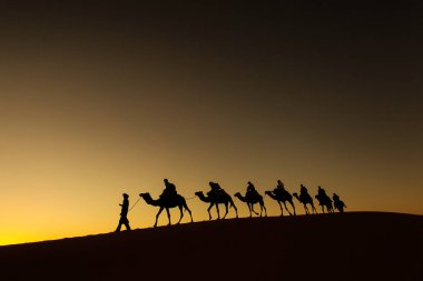 Sillhouette mutlu peopple ile arka planda kızıl gökyüzü gün batımında çölde gidiş ile deve karavan