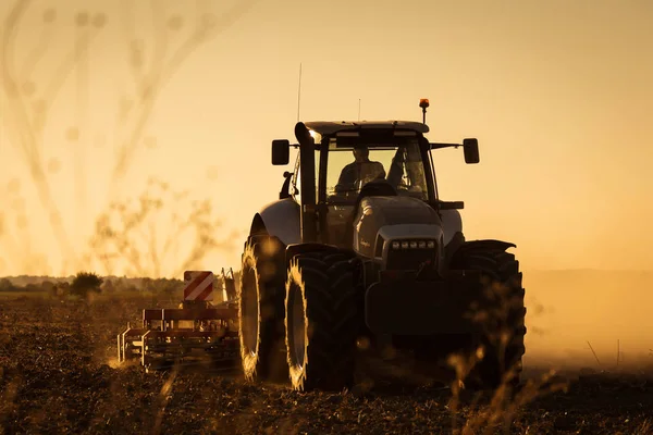 现代拖拉机在日落时耕耘 背景中有大量灰尘 — 图库照片