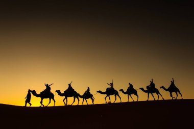 Sillhouette mutlu peopple ile arka planda kızıl gökyüzü gün batımında çölde gidiş ile deve karavan