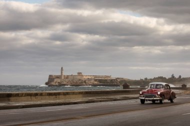 Havana 'nın Malecon caddesinde, arkasında fırtına bulutları olan eski bir araba. Küba