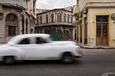 Havana sokaklarında eski bir araba. Arkasında renkli binalar var. Küba