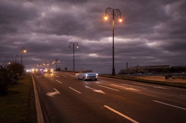 Havana 'nın Malecon caddesinde, arkasında fırtına bulutları olan eski bir araba. Küba