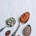 Top view of group of spices in spoons on white table