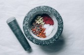 top view of mortar with spices and pestle on white table