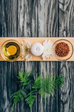 top view of arranged oil, scrab, candle and chrysanthemum flowers for spa and massage on wooden tabletop clipart