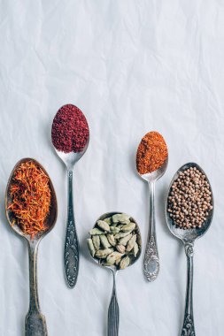 elevated view of different spices in spoons on white table clipart