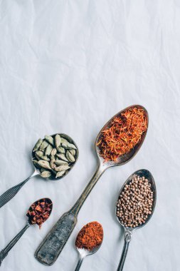 top view of group of spices in spoons on white table clipart