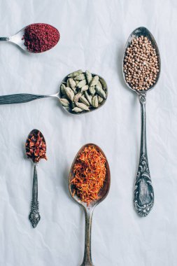 top view of coriander, chilli flakes and saffron in spoons on white table clipart