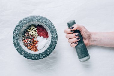cropped image of woman holding pestle near mortar with spices on white table clipart