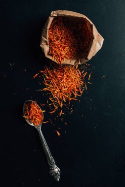 top view of red saffron in paper bag and spoon on table clipart