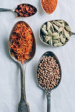 top view of different spices in spoons on white table clipart