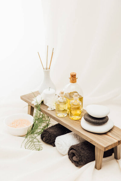 close up view of arrangement of spa treatment accessories with towels, oil and salt on white background